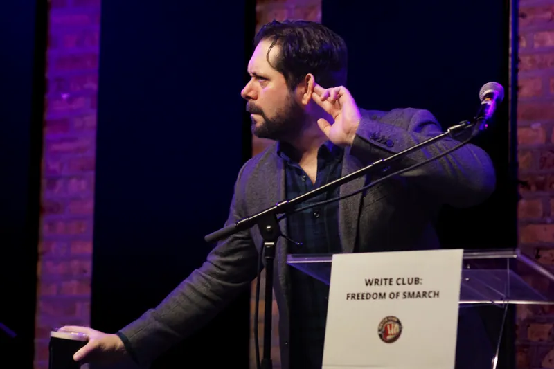 A combatant leaning into the microphone with a hand cupped to his ear