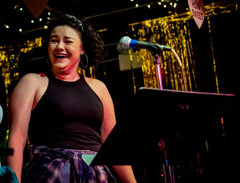 A performer laughing at the microphone in front of gold tinsel