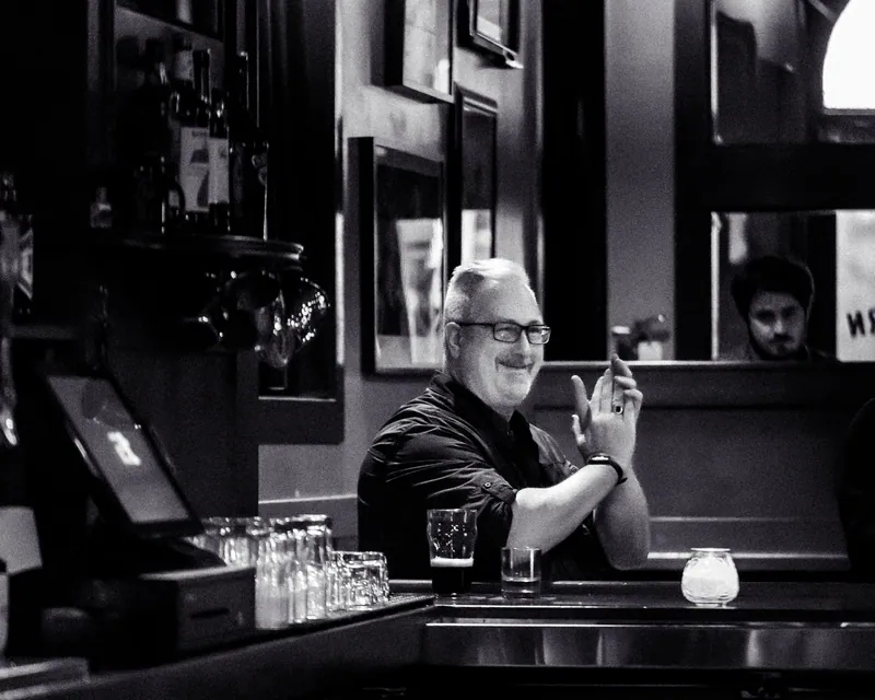 A host seated at the bar between bouts, in black and white