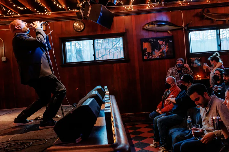 Wide shot of the room, a combatant at the microphone and the crowd along the back wall
