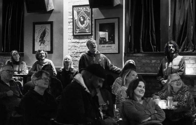 The crowd at the tables, heads back laughing, in black and white