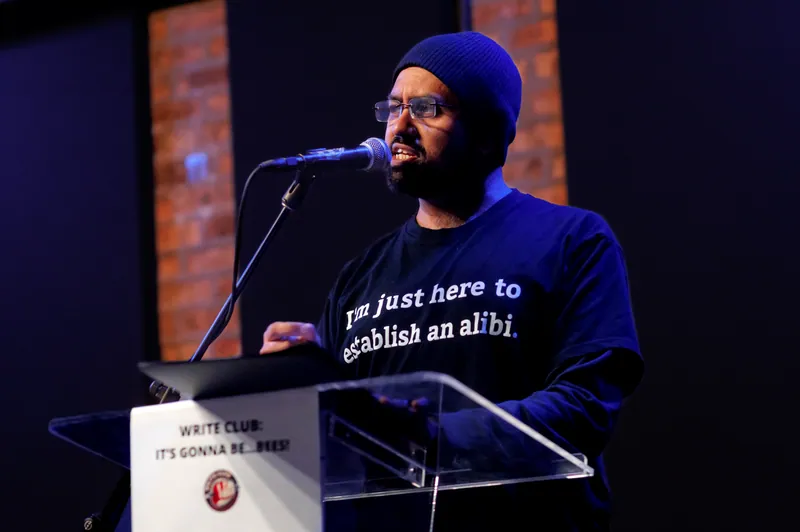 A combatant in a beanie at the lectern, his shirt reading I'm just here to establish an alibi