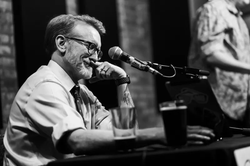 The host at the microphone with a pint on the table, in black and white