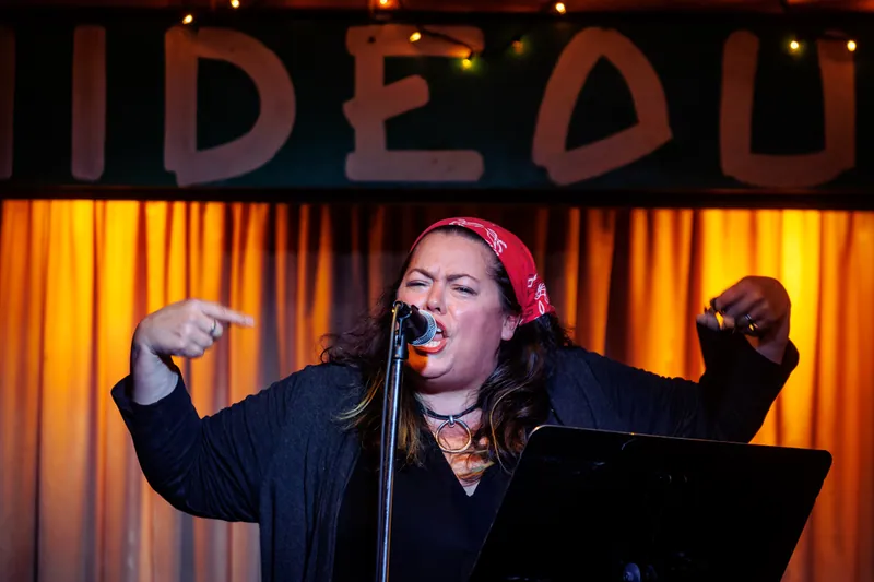 A combatant on stage with both arms out, wearing a red bandana