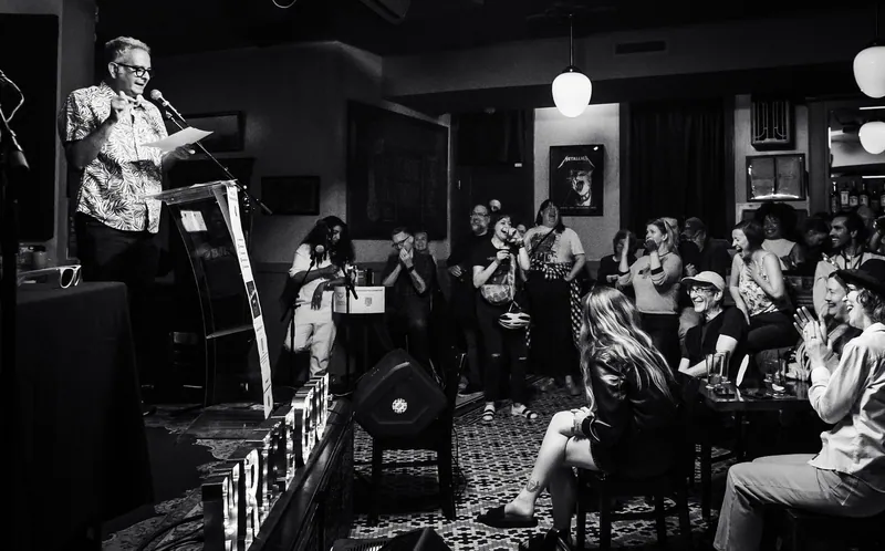 The room from the back, a host at the lectern and a full house, in black and white